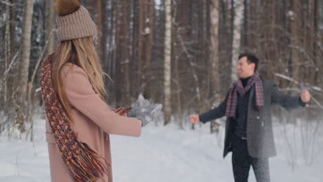 A-young-man-and-a-woman-in-a-coat-are-having-fun-and-playing-with-snow-in-a-winter-forest-in-slow-motion.-Happiness-and-smiles-on-faces